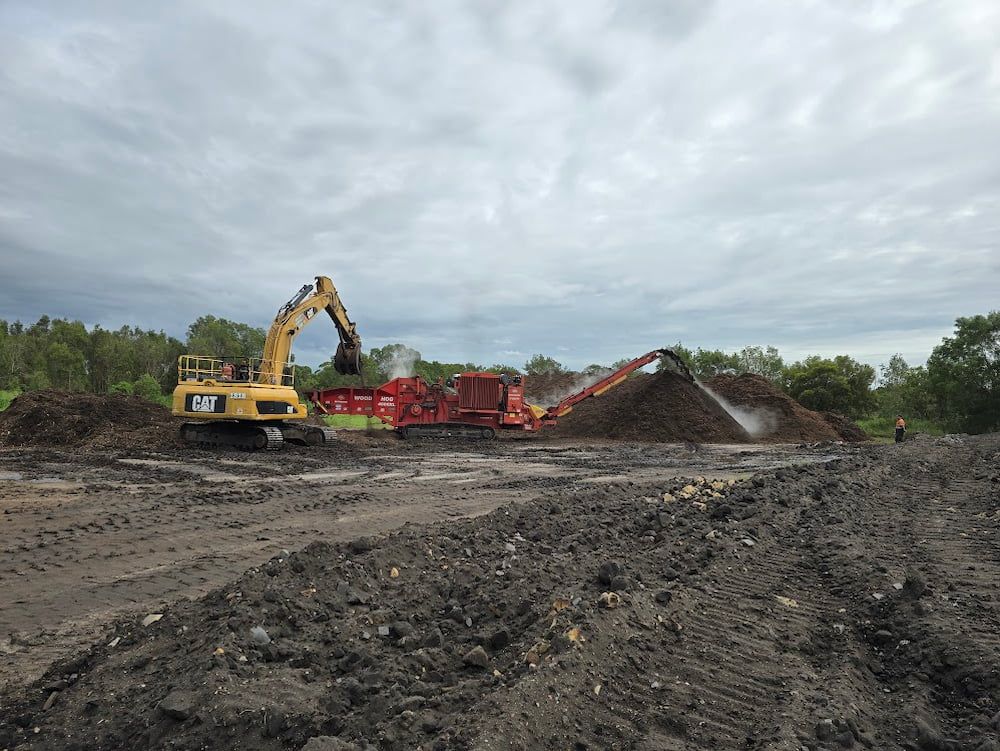 Yellow Excavator Loading a Woodchipper — Coastal Sand Soil & Mulch in Craignish, QLD