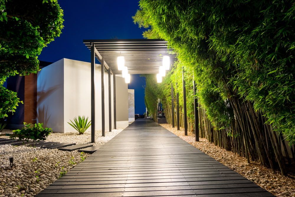 Wooden walkway under a canopy with hanging lights, flanked by bamboo and a white building at night. — Coastal Sand Soil & Mulch in Point Vernon, QLD