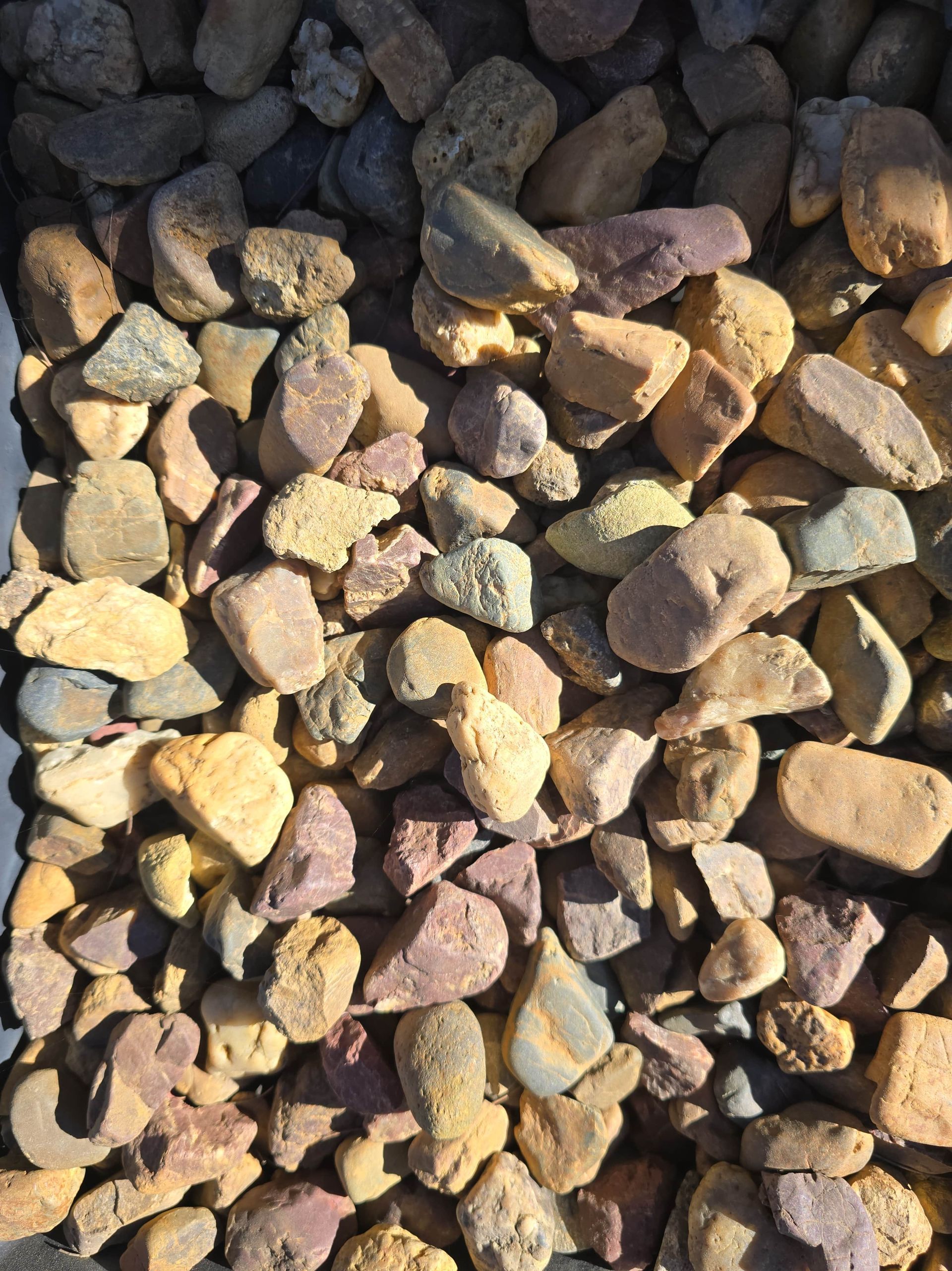 Close-up of a pile of smooth, multi-coloured river rocks — Coastal Sand Soil & Mulch in Craignish, QLD
