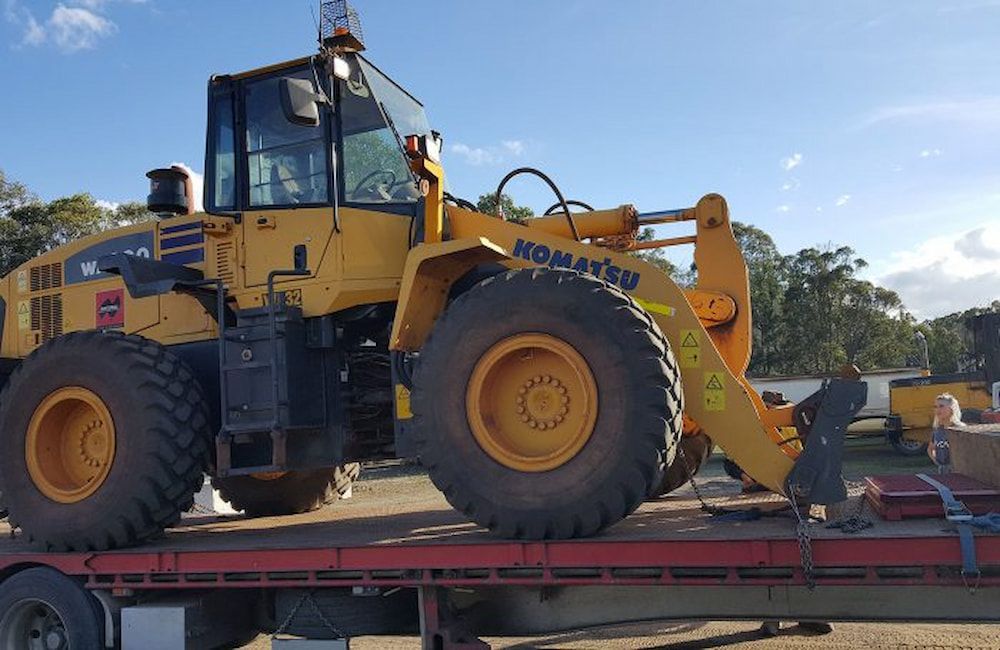Yellow Komatsu Loader on a Red Flatbed Trailer, Outdoors — Coastal Sand Soil & Mulch in Craignish, QLD