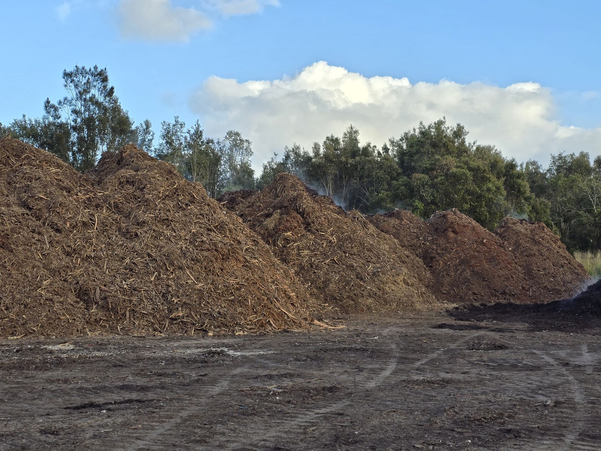 Piles of wood chips on a dark, dusty ground — Coastal Sand Soil & Mulch in Craignish, QLD