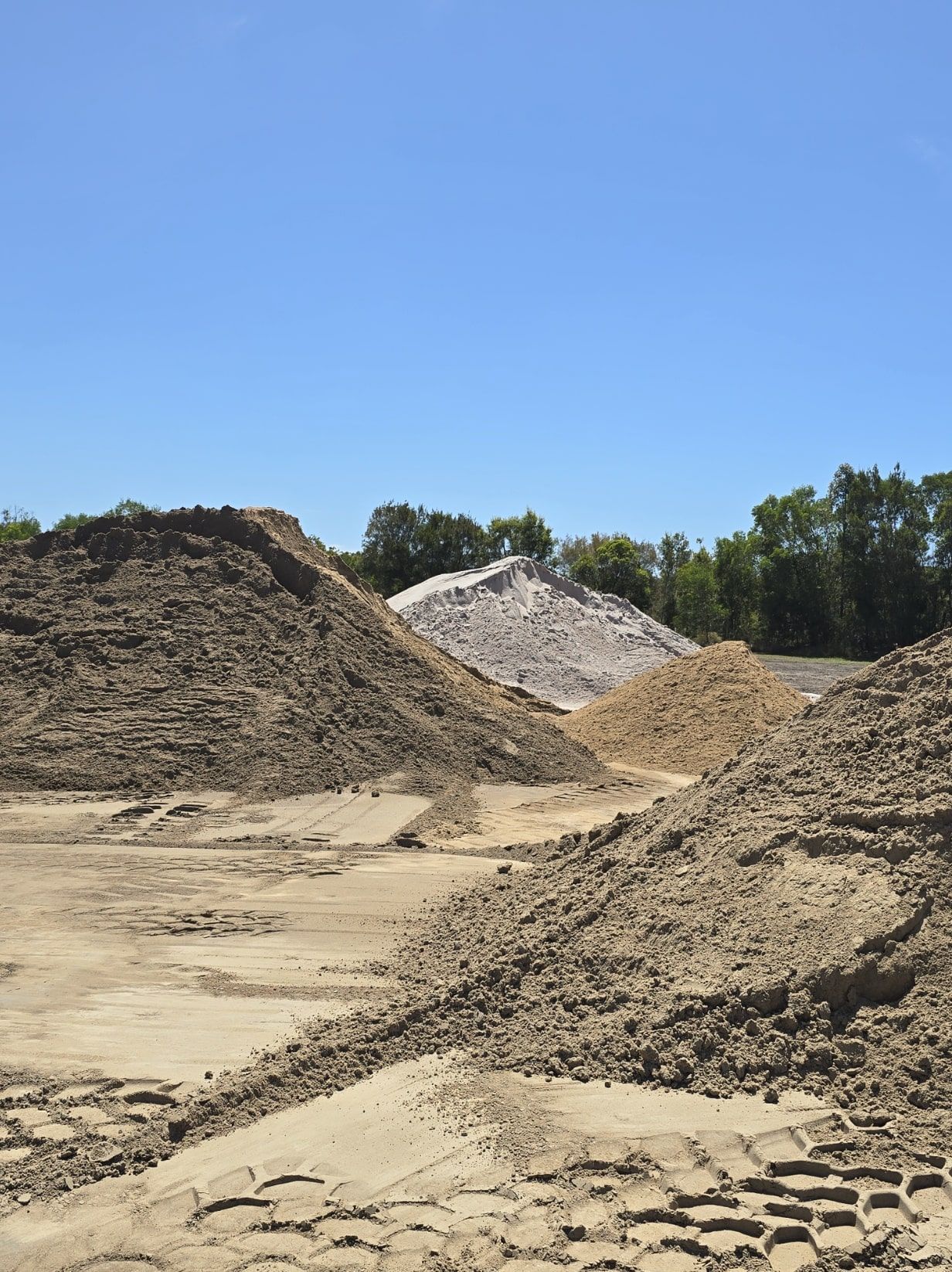 Piles of sand and gravel outdoors on a sunny day — Coastal Sand Soil & Mulch in Craignish, QLD