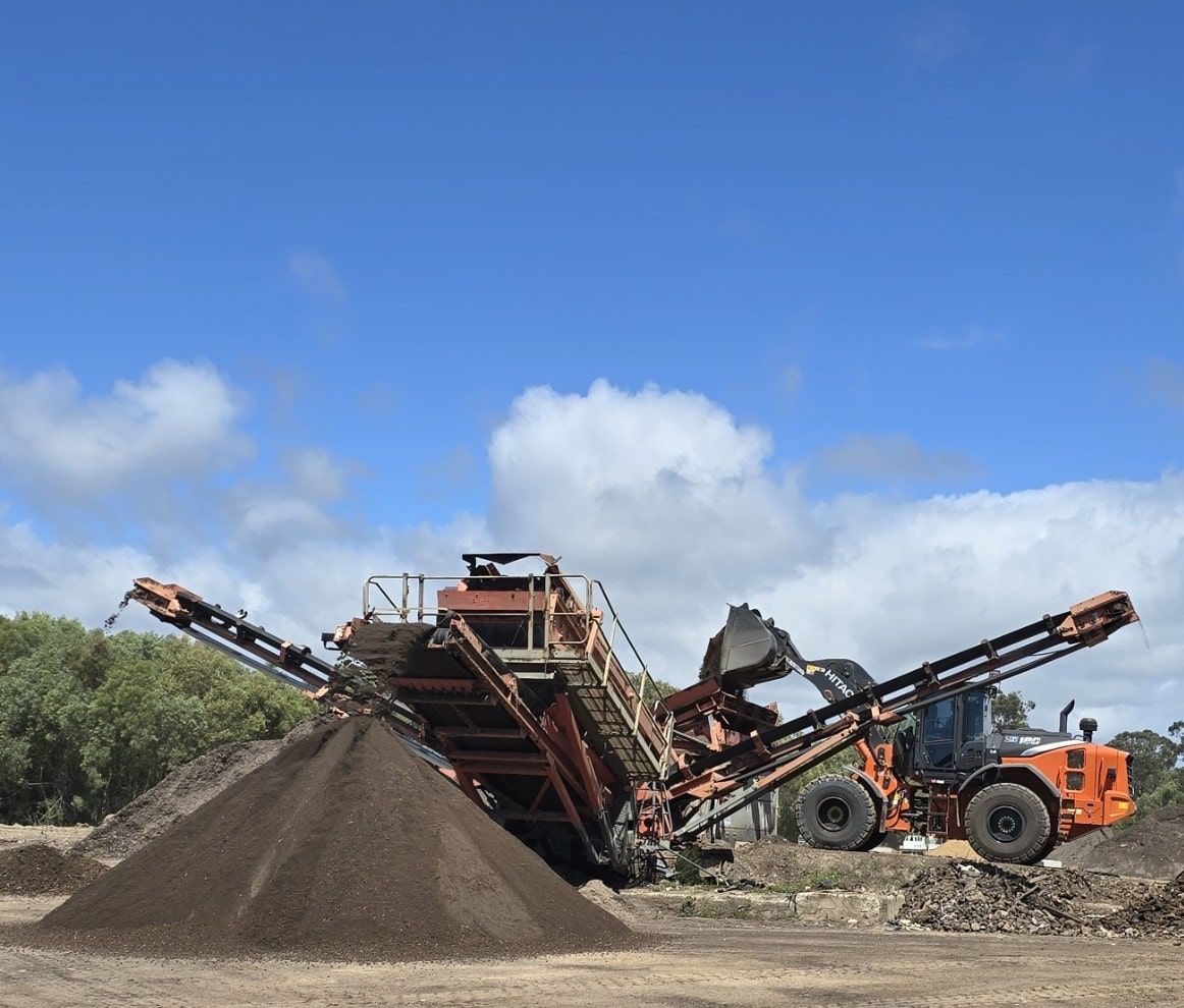 A large orange tractor sifting a pile of dark compost against a blue sky — Coastal Sand Soil & Mulch in Craignish, QLD