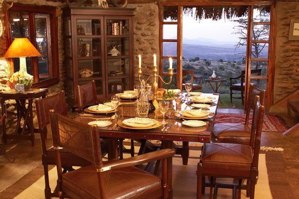 Golf shop fixtures adjacent to a dining room setting, with a table prepared for a meal, framed by a stone wall and open doors revealing a natural view.