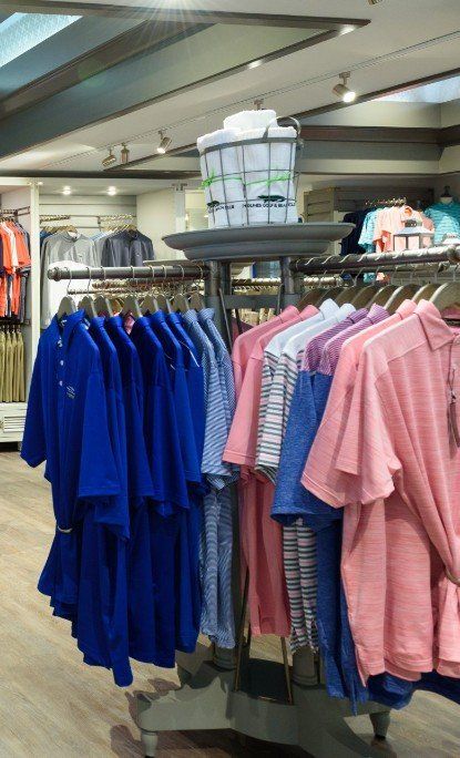 Pro shop fixtures displaying rows of brightly colored polo shirts, including blue, pink, and patterned styles on clothing racks.
