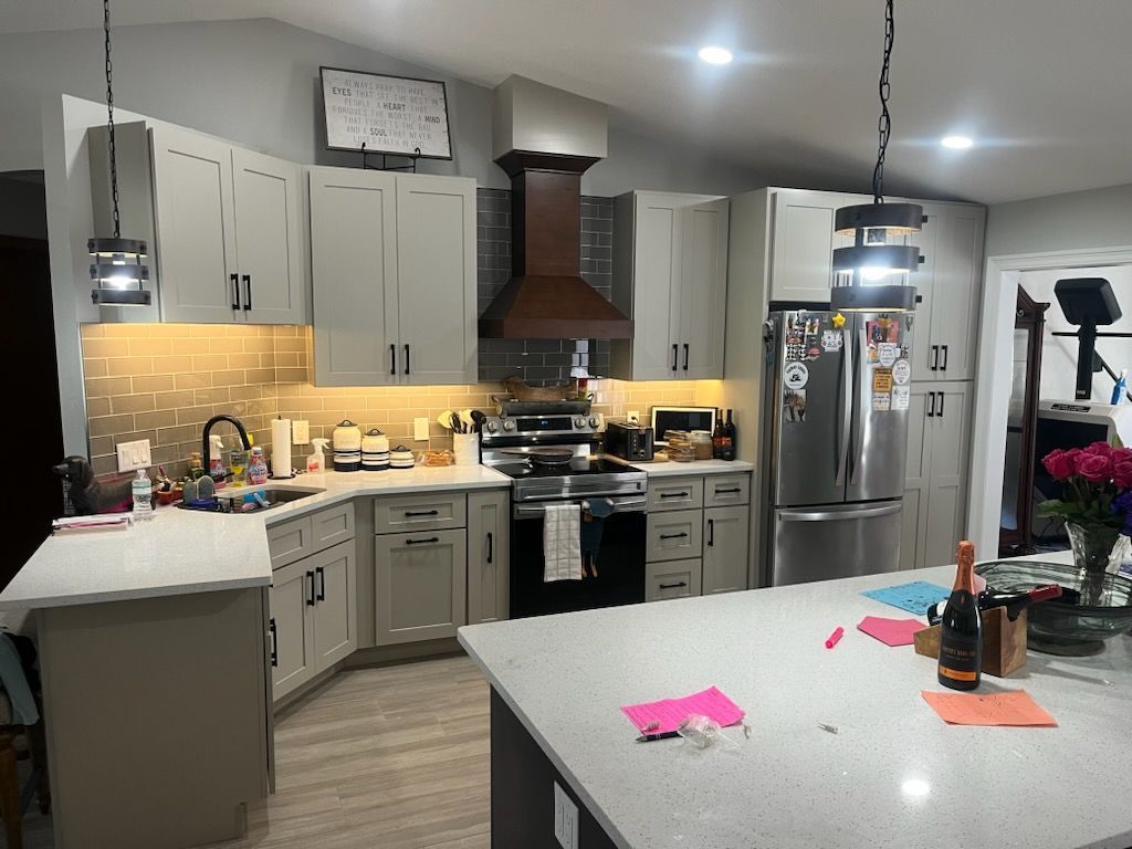 A modern kitchen with light gray cabinets, a large central island, stainless steel appliances, and a wood range hood.