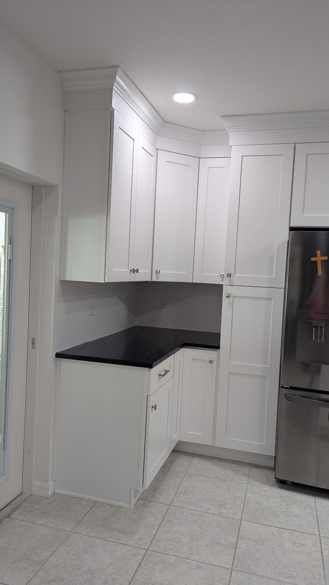 White kitchen cabinets with black countertops and a stainless steel refrigerator in a room with light patterned tile floors.