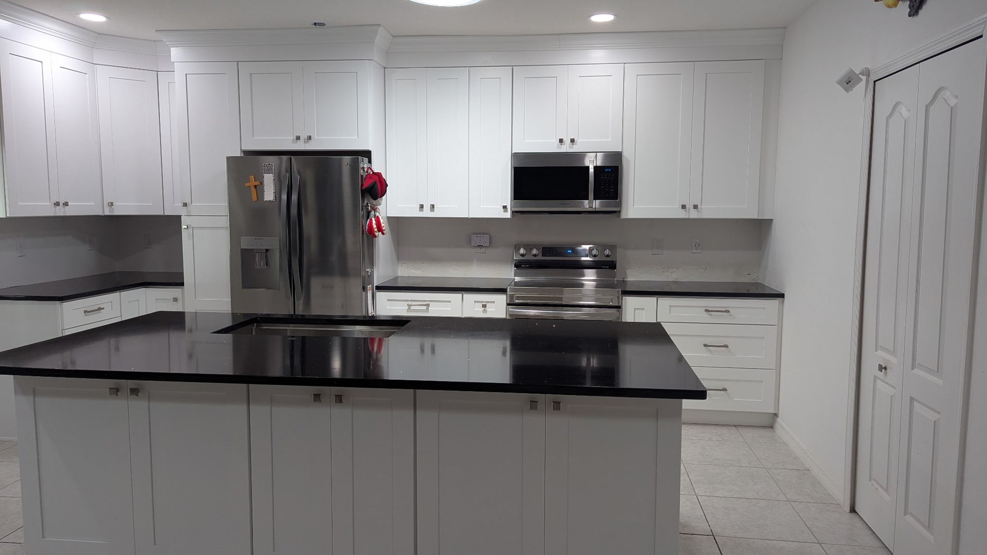 A bright, modern kitchen featuring white shaker cabinets, a large island with a black countertop, and stainless appliances.