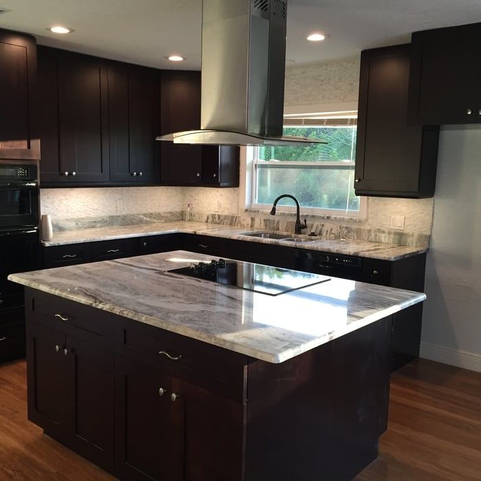 Modern kitchen with dark cabinets, a marble-topped island with a cooktop, and a stainless steel range hood.