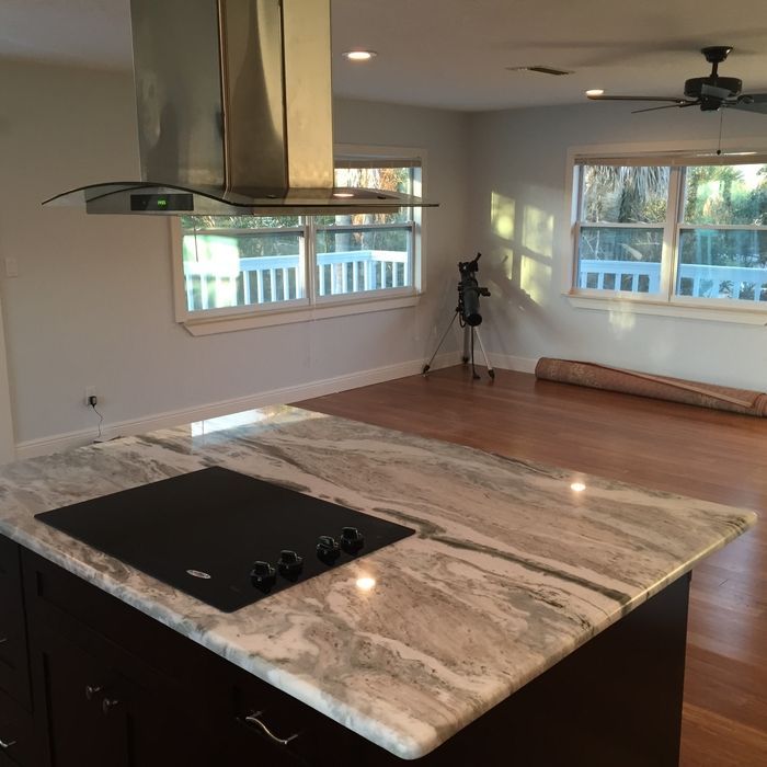 A kitchen island with a marble countertop and cooktop, centered in a room with hardwood floors and large windows.