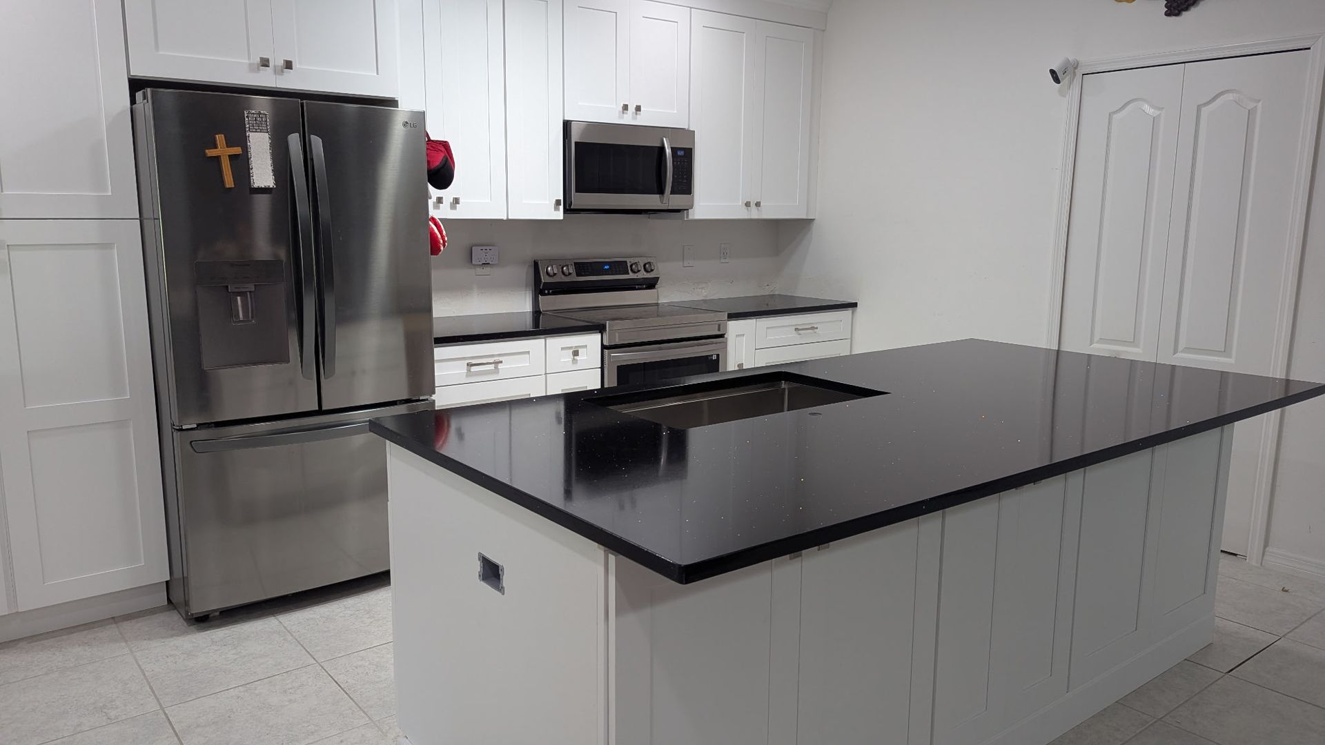 A modern kitchen with white cabinetry, stainless steel appliances, and a large central island with a black countertop.