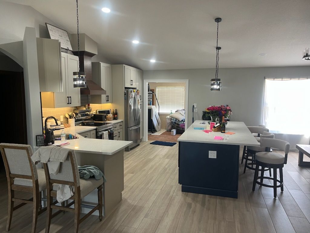 A spacious kitchen with a dark blue island, light-colored countertops, white cabinetry, and tall chairs on wood-look floors.
