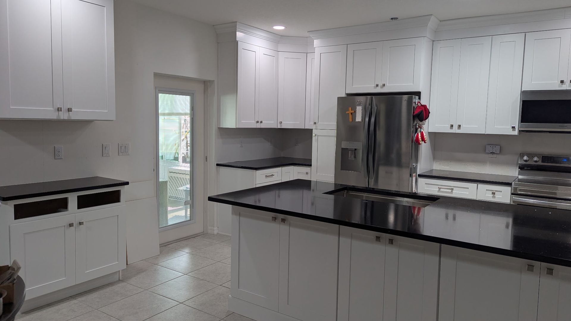 A white kitchen featuring black countertops, stainless steel appliances, and a central island.