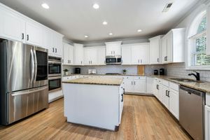 White kitchen with stainless steel appliances, granite countertops, and light wood flooring.
