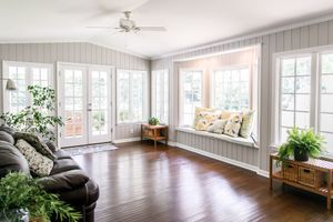 Sunroom with dark wood floors, white trim, a window seat with pillows, and a leather couch.
