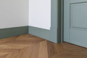 Herringbone wood floor, white walls, and a blue-green trim meet at a corner, next to a matching door frame.