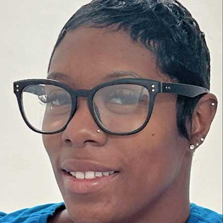 A woman wearing a white shirt and a necklace is smiling for the camera.
