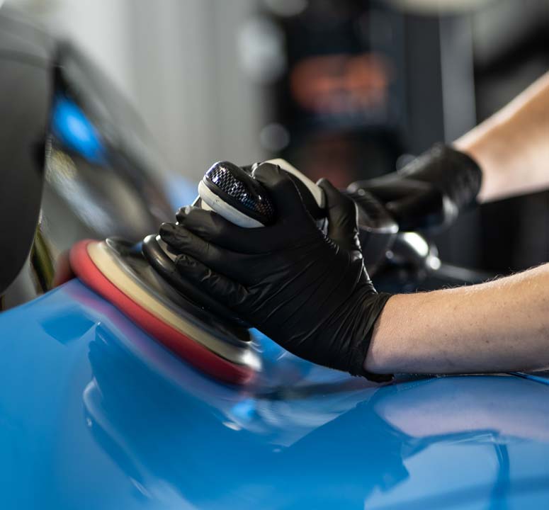 A person wearing black gloves is polishing a blue car