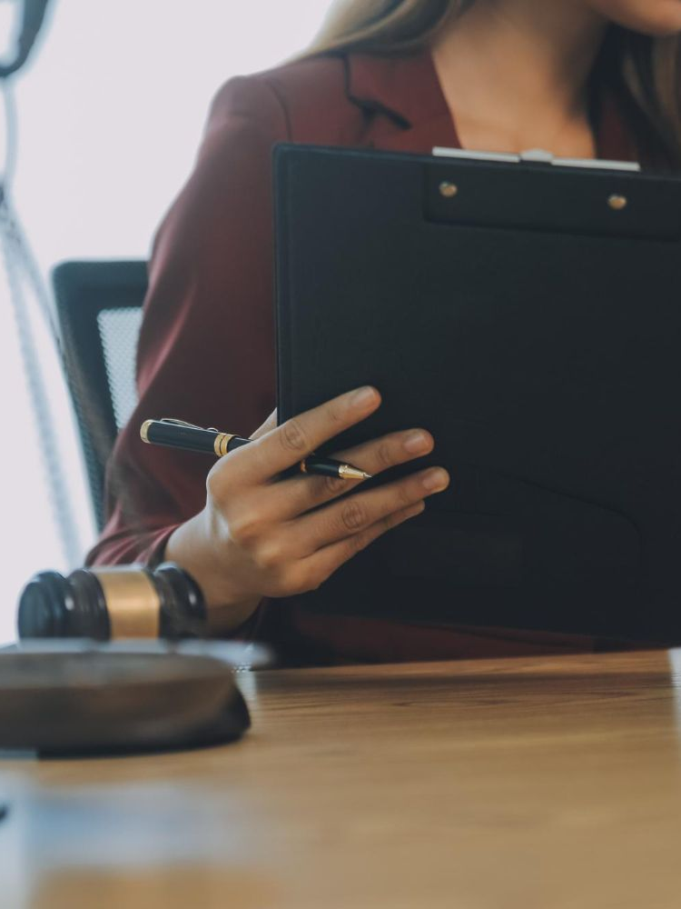 Person in red blazer holding a clipboard and pen near a wooden gavel.