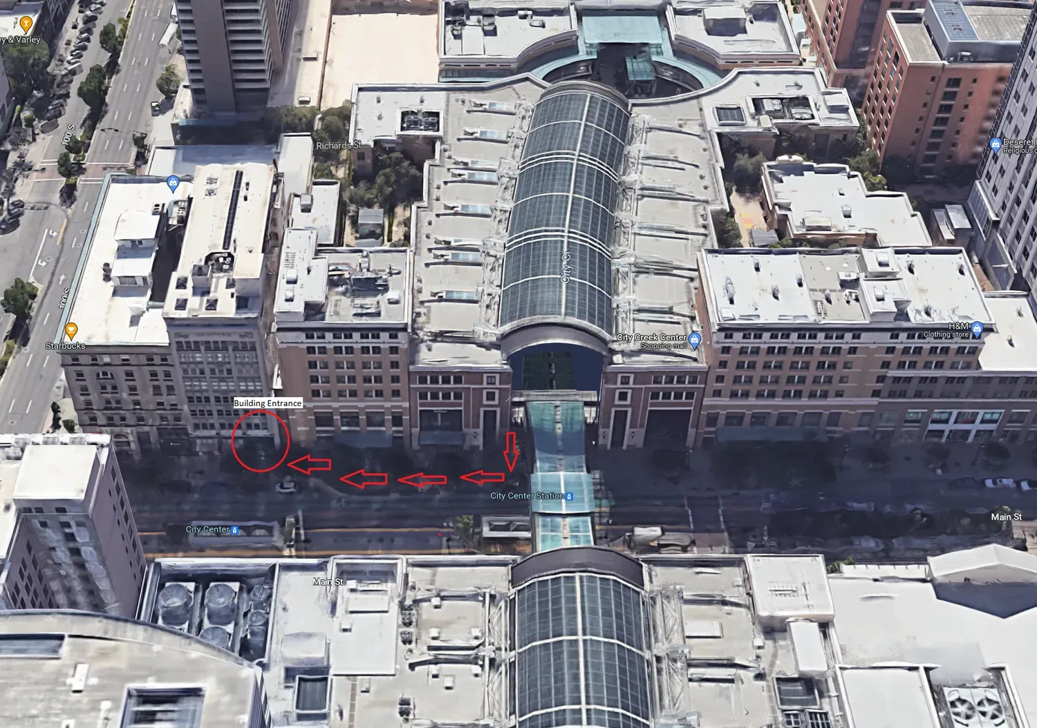 Aerial view of an urban plaza with a glass-covered walkway connecting two brick buildings across a street.