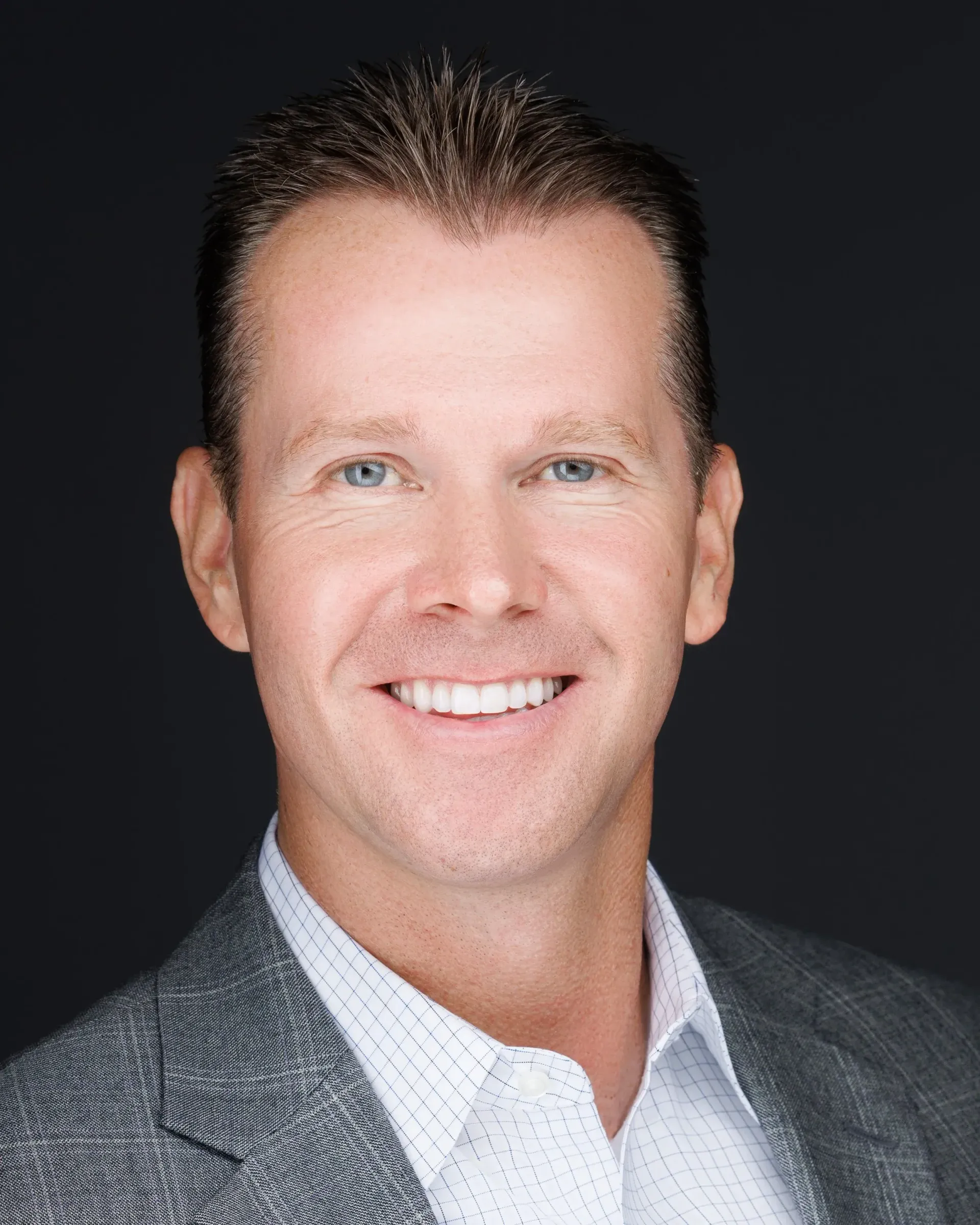 Woman with dark hair, smiling, in a floral shirt, seated indoors with a framed artwork in the background.