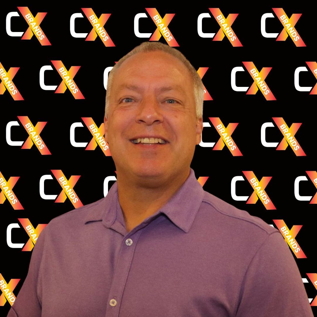 A man in a purple shirt is smiling in front of a sign that says expo