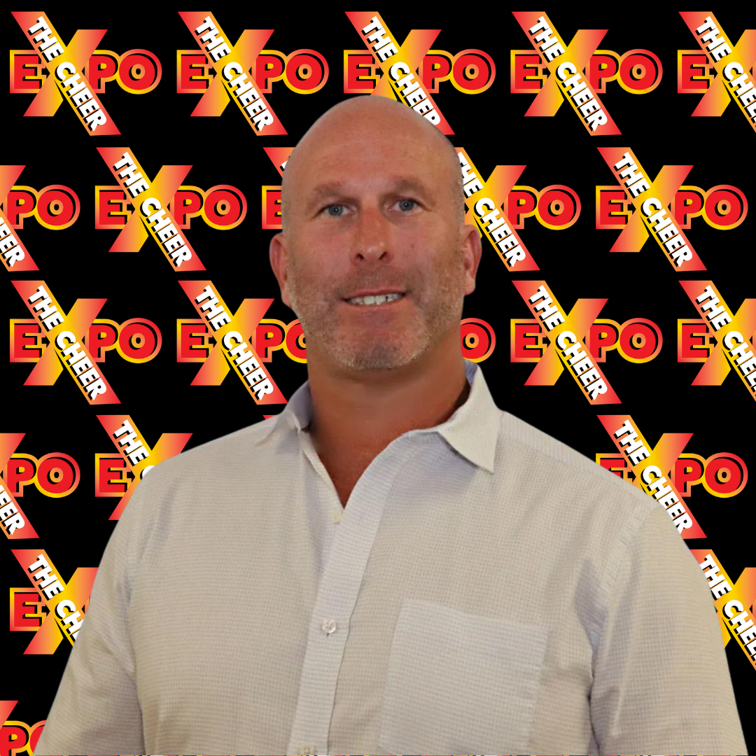 A bald man in a white shirt stands in front of a black background with the word expo on it