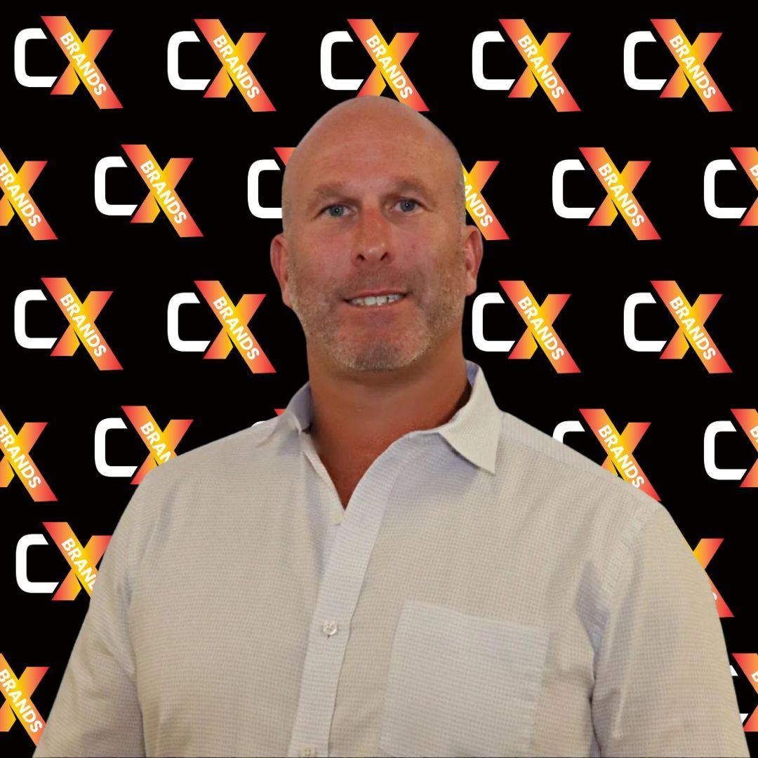 A bald man in a white shirt stands in front of a black background with the word expo on it