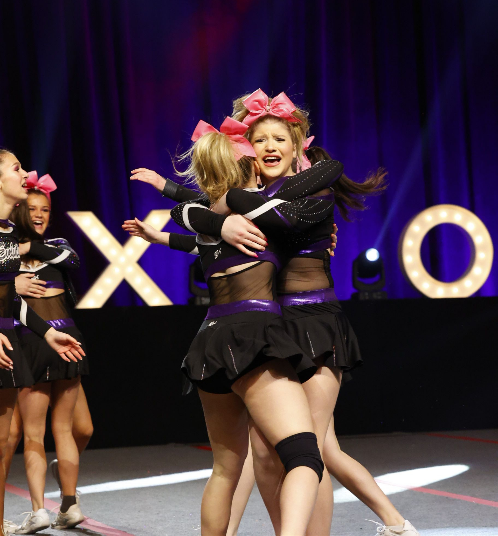 A group of cheerleaders are hugging in front of a sign that says xoxo