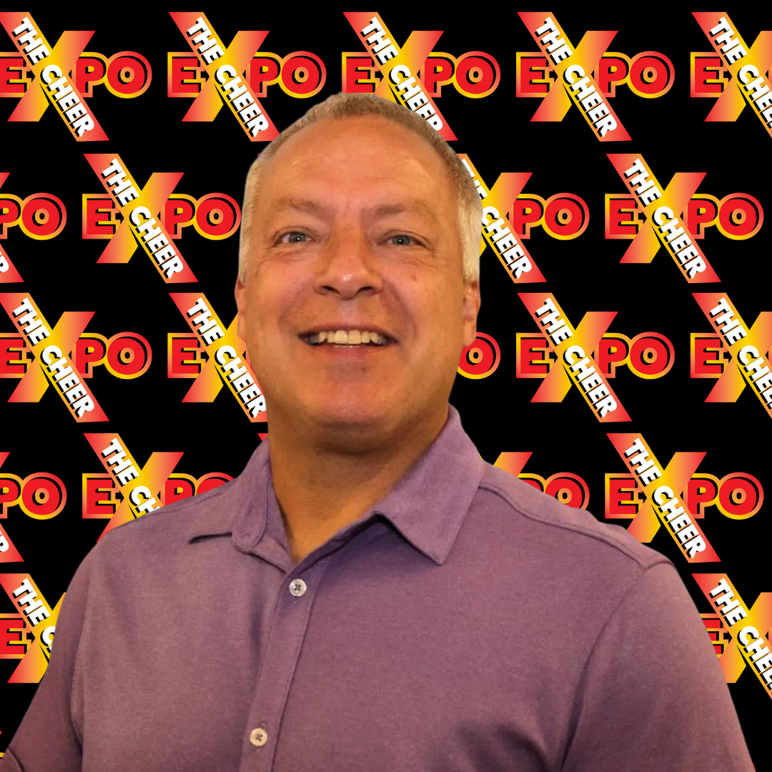 A man in a purple shirt is smiling in front of a sign that says expo