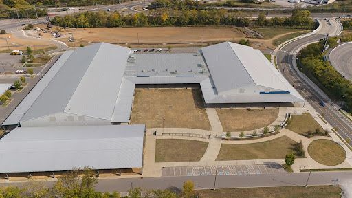 An aerial view of a large building with a gray roof surrounded by trees.