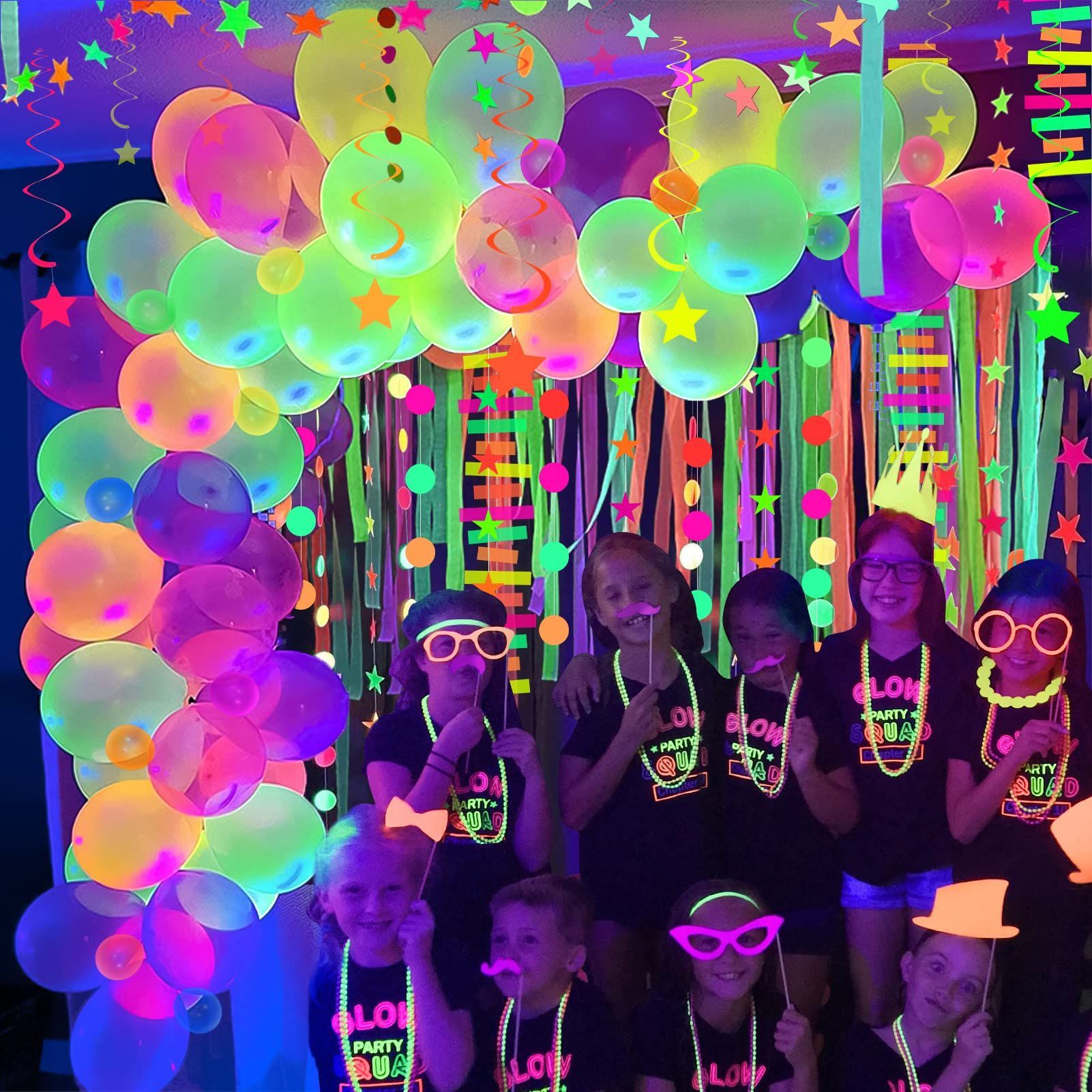 A group of children are posing for a picture in front of glow in the dark balloons