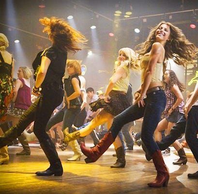 A group of people are dancing on a stage and one woman is wearing cowboy boots