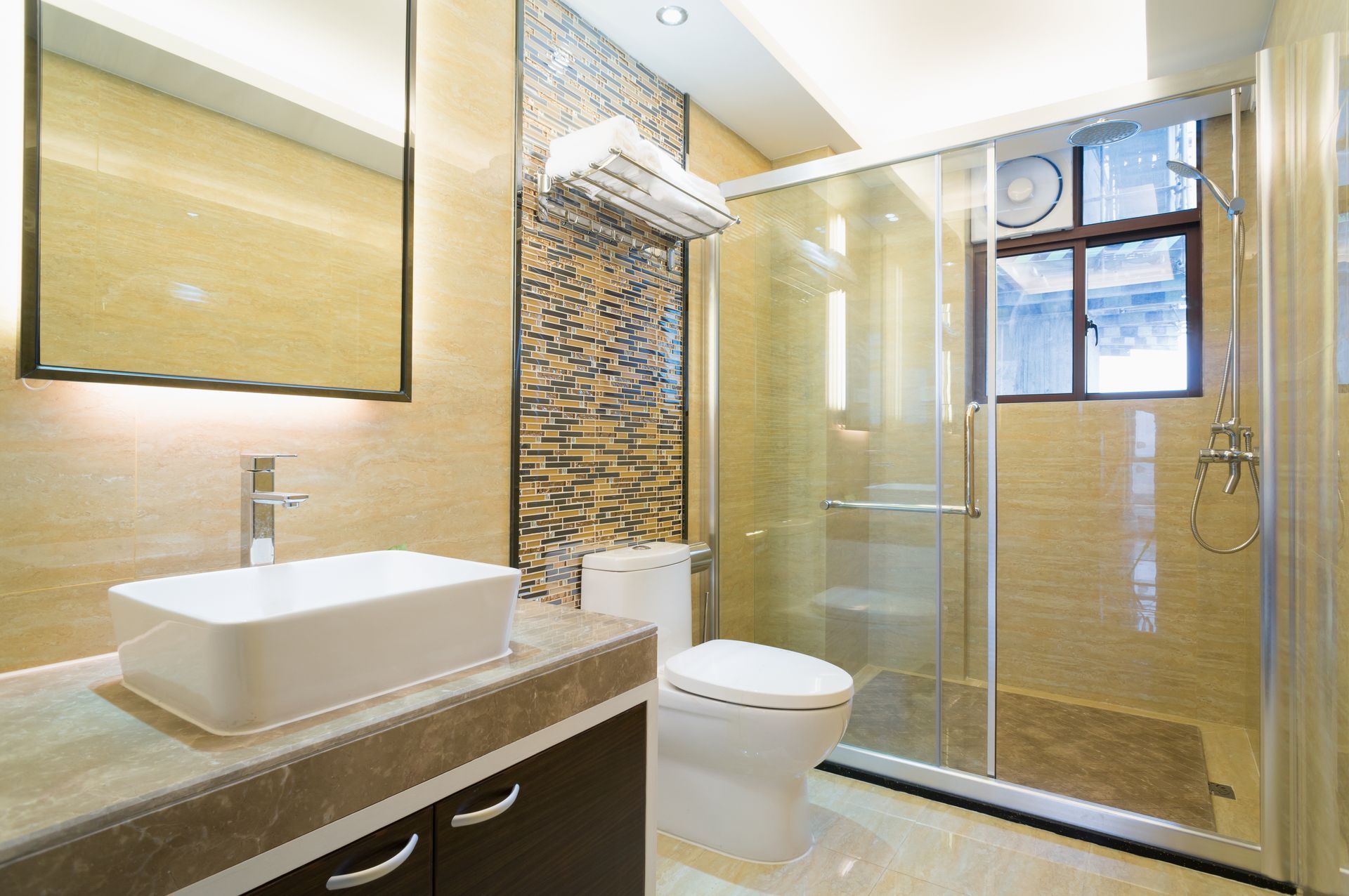 Bathroom with a white sink, toilet, and glass shower. Beige tiles and a decorative wall.
