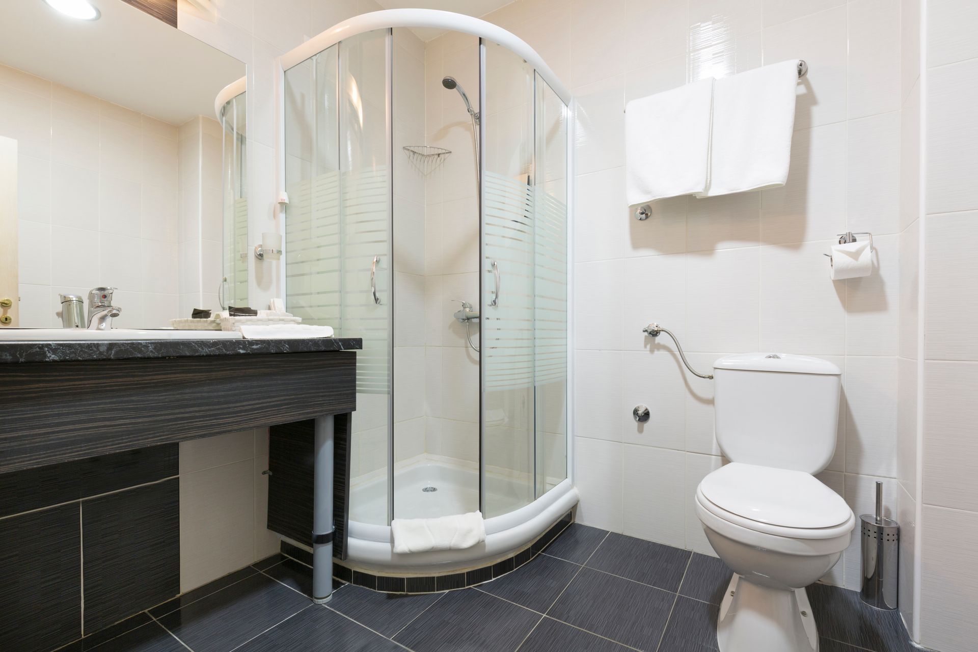 Bathroom with a curved glass shower, toilet, sink, and white towels on a towel rack.