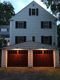 Two-story white house with attached two-car garage. Brown garage doors are illuminated at dusk.