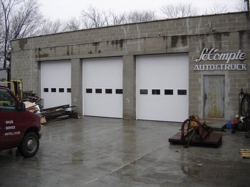 Exterior of LeCompte Auto & Truck with three white garage doors and a red van parked on the left.