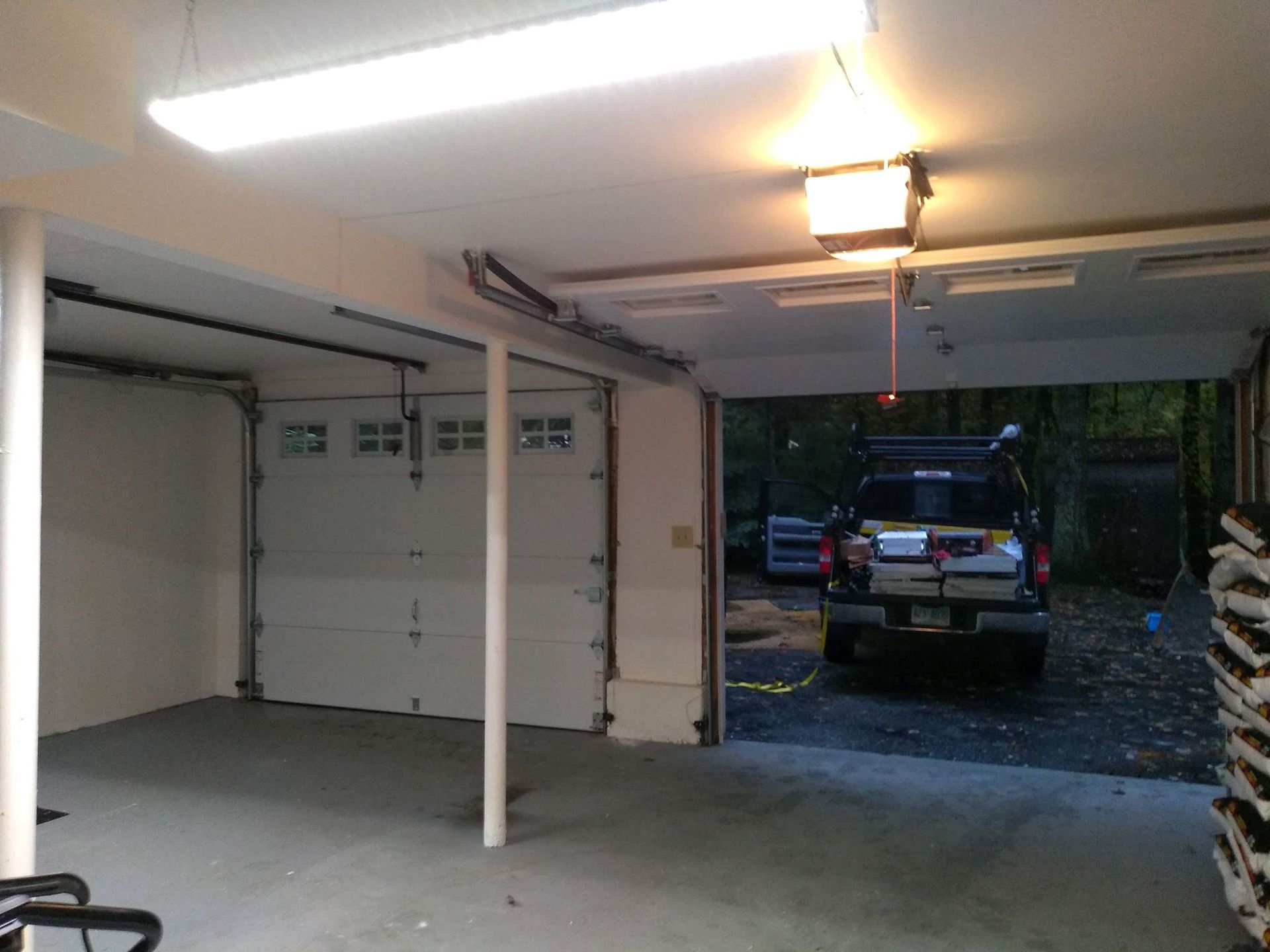 Garage interior with open door, parked truck, white door, bright lighting, and concrete floor.