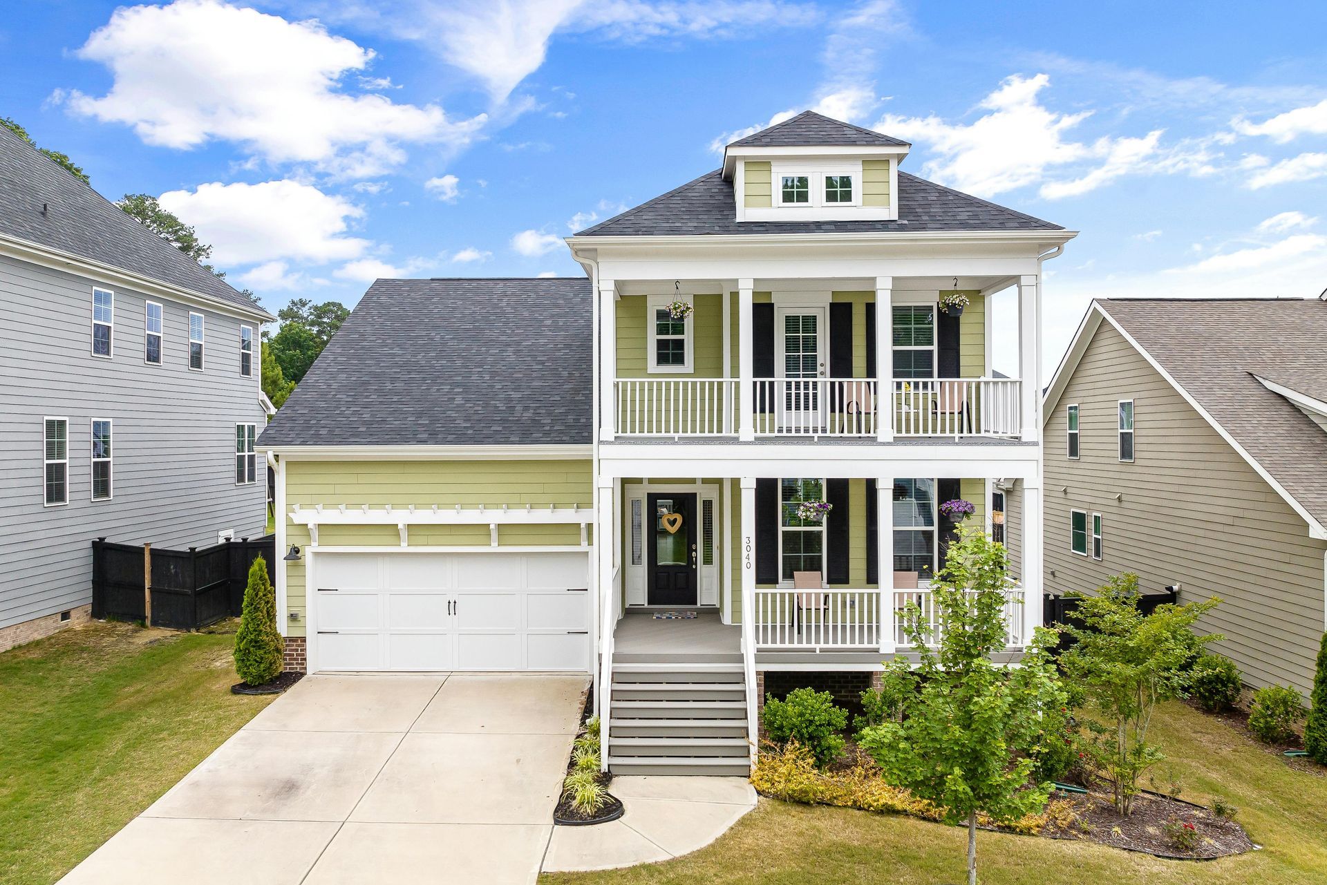 Two-story house with green siding, white trim, and a porch. The house has a gray roof and a two-car garage.