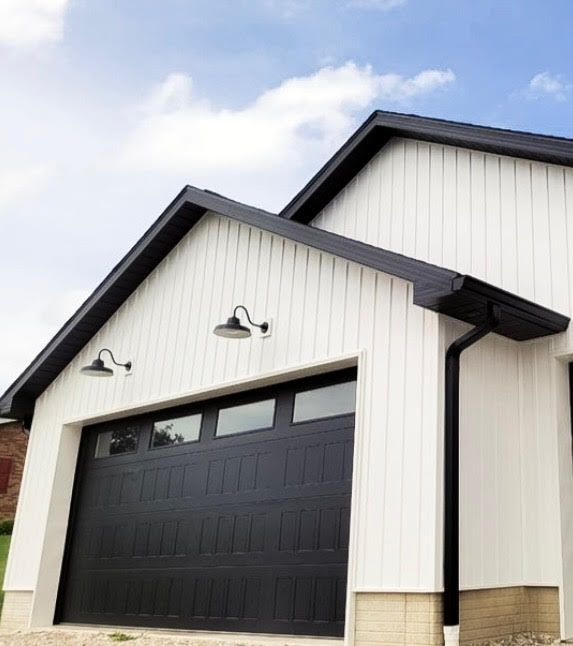 White garage with a black door and trim; two lights, blue sky.