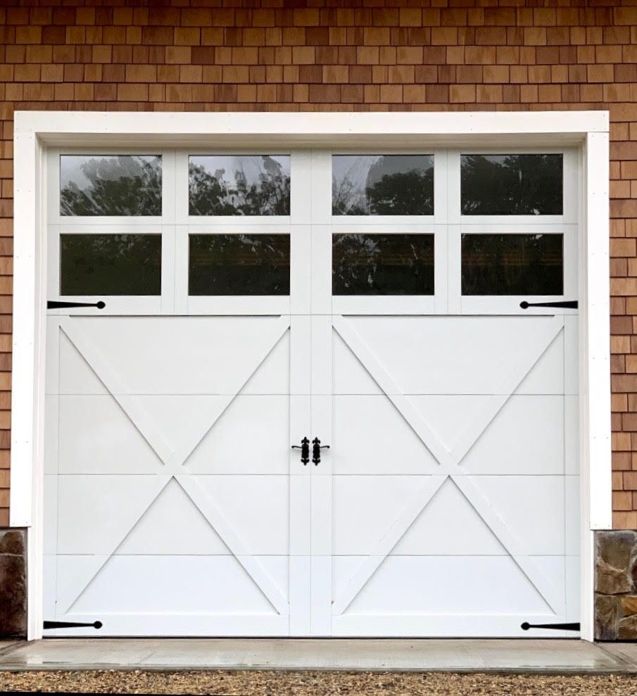 White garage door with window panes, decorative black hardware, and brick exterior.