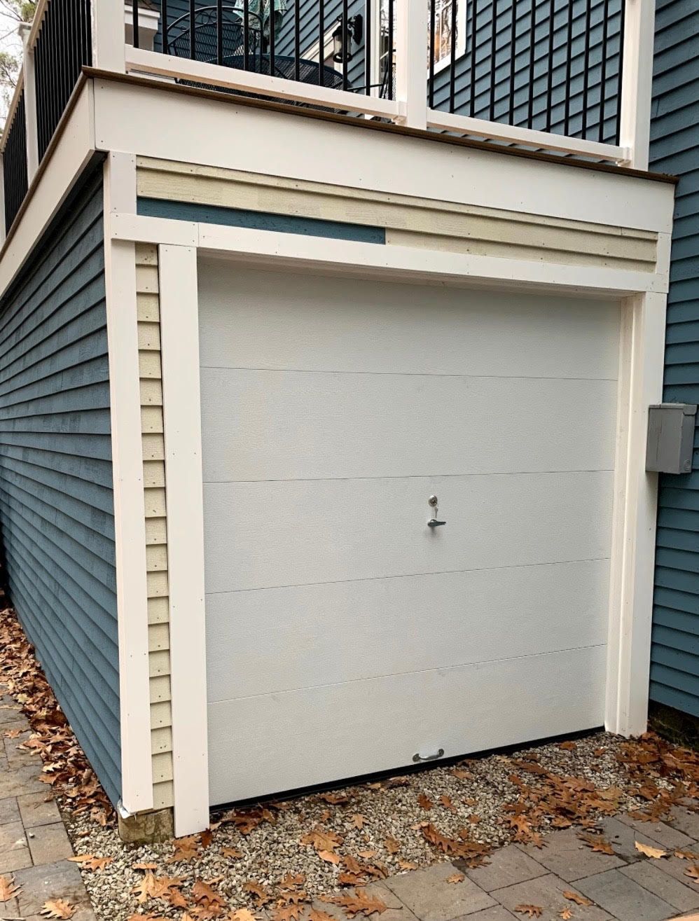 White garage door in a blue-sided building with cream trim and an upper deck.