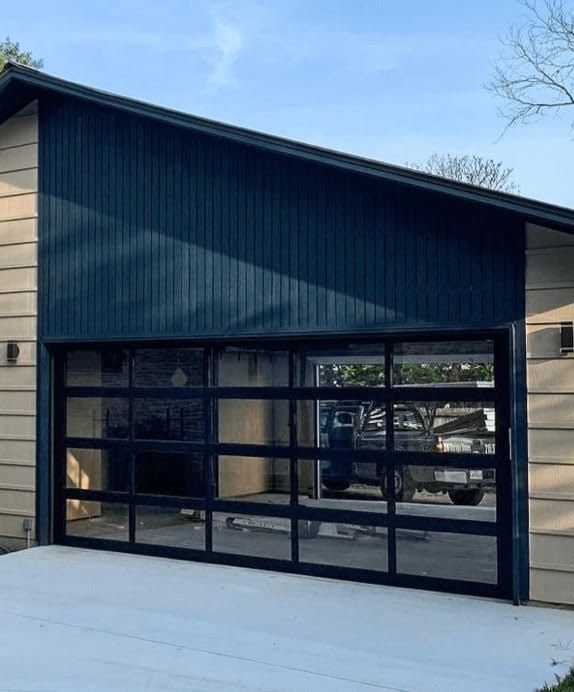 Modern garage with black-framed glass door, dark blue siding, and tan horizontal siding.