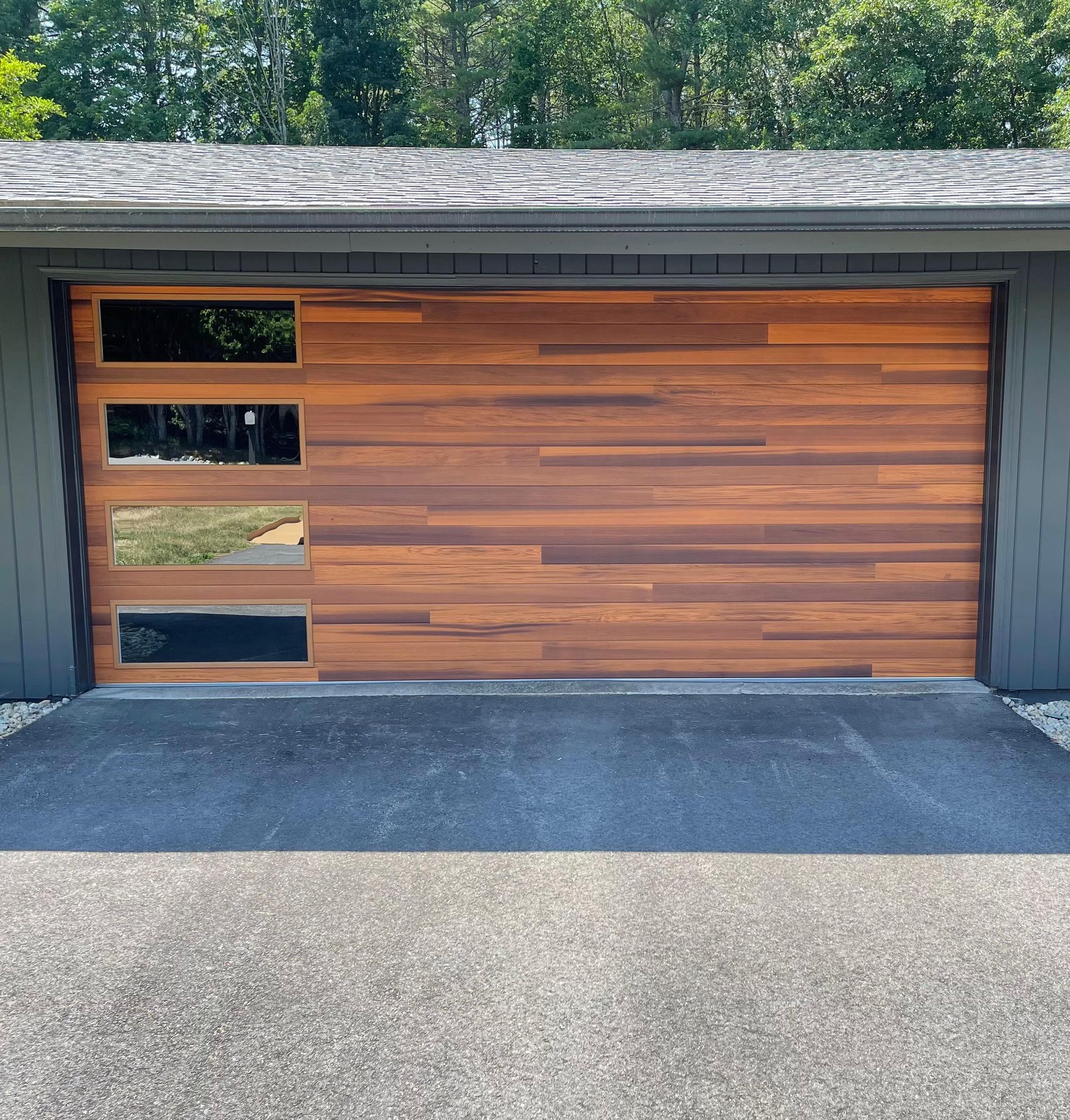 Wooden garage door with three rectangular windows, set in a gray frame, on a gray asphalt driveway.