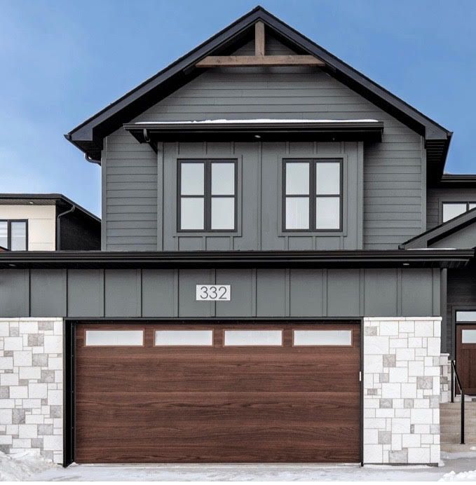 Modern two-story house with gray siding, a wooden garage door, and stone accents.
