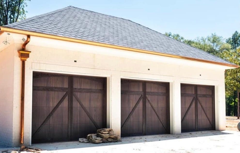 Three-bay garage with dark brown doors, light walls, and a gray roof with copper gutters.