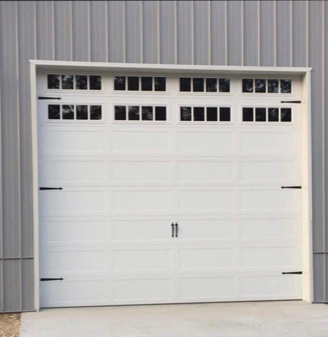 White garage door with window panels and black hardware, set against a grey metal building.