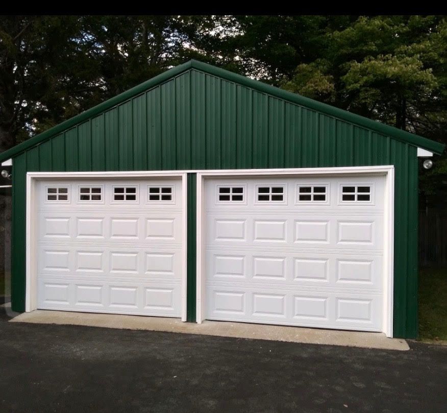 Green metal-sided garage with two white garage doors, set against a backdrop of trees.