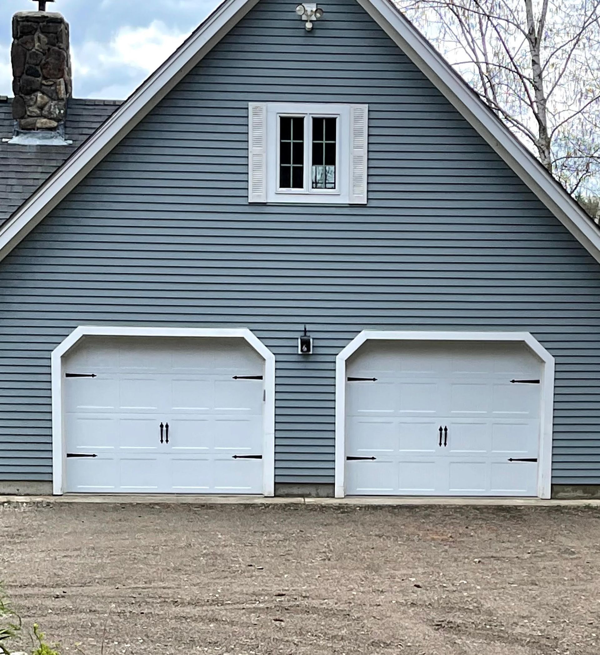 Blue-sided garage with two white doors and a small window above. A stone chimney is to the left.