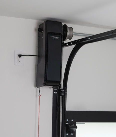 Garage door opener mounted on a white wall, black unit with red emergency cord.